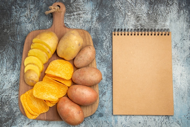 Photo gratuite vue de dessus des chips croustillantes et pommes de terre non cuites sur planche à découper en bois et ordinateur portable sur fond gris