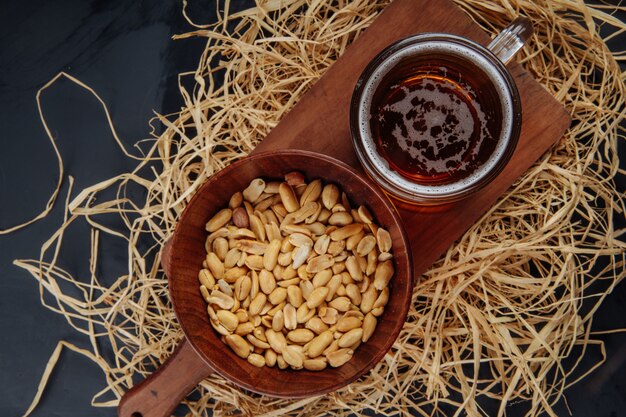 Vue de dessus d'une chope de bière et d'arachides dans un bol sur une planche de bois sur de la paille sur noir jpg