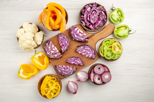 Vue de dessus chou rouge haché sur planche de bois coupé tomates vertes coupées en pupmkin couper les poivrons jaunes dans des bols sur une surface blanche