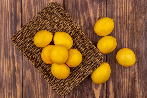 Vue de dessus des citrons d'agrumes sur un plateau en osier avec des citrons isolés sur un mur en bois