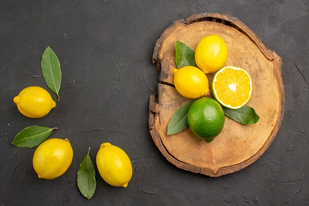 Vue de dessus citrons aigres frais avec des feuilles sur la table sombre fruits citron vert citron jaune