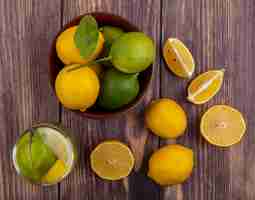 Photo gratuite vue de dessus citrons aux limes dans un bol et verre d'eau de désintoxication sur fond de bois