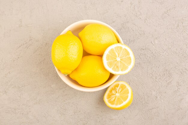 Une vue de dessus des citrons frais aigre mûr entier moelleux agrumes tropical vitamine jaune avec des fleurs séchées sur le bureau de la crème