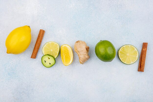 Vue de dessus de citrons frais et colorés avec des bâtons de cannelle au gingembre avec des tranches de concombre sur blanc