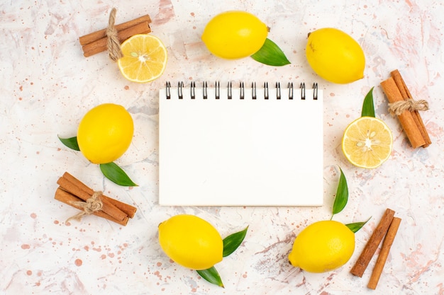 Photo gratuite vue de dessus citrons frais dans une forme de cercle citrons coupés bâtons de cannelle cahier sur une surface isolée lumineuse