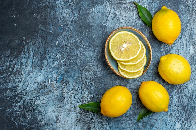 Vue de dessus des citrons frais entiers et coupés avec des feuilles sur le côté gauche sur fond sombre