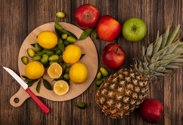 Vue de dessus des citrons frais isolés sur une planche de cuisine en bois avec des pommes et des ananas isolés sur une surface en bois