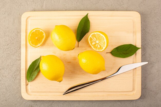 Une vue de dessus des citrons frais jaunes mûrs moelleux juteux avec des feuilles vertes refait surface sur le bureau crème doublé et tranché sur le fond gris fruits couleur agrumes