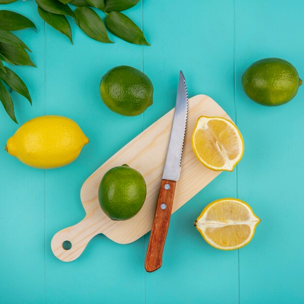 Vue de dessus des citrons frais sur planche de cuisine en bois avec couteau et feuilles sur bleu