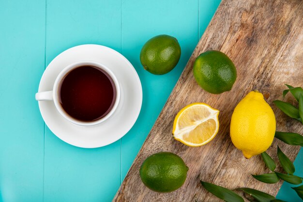 Vue de dessus des citrons frais sur planche de cuisine en bois avec une tasse de thé sur bleu