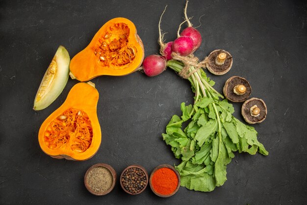 Vue de dessus de la citrouille fraîche avec des verts et des radis sur un bureau sombre