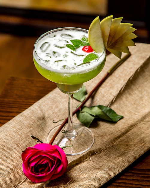 Vue de dessus cocktail vert avec de la glace et décor avec des tranches de cerise menthe pomme et rose rose sur la table