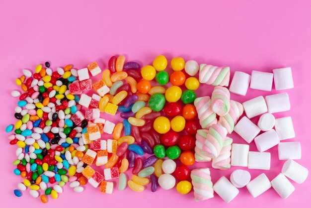 Une vue de dessus composition de bonbons colorés de différentes couleurs de bonbons sucrés et délicieux sur un bureau rose