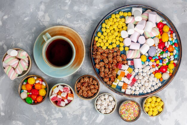 Vue de dessus de la composition de bonbons différents bonbons colorés avec de la guimauve et une tasse de thé sur un bureau blanc