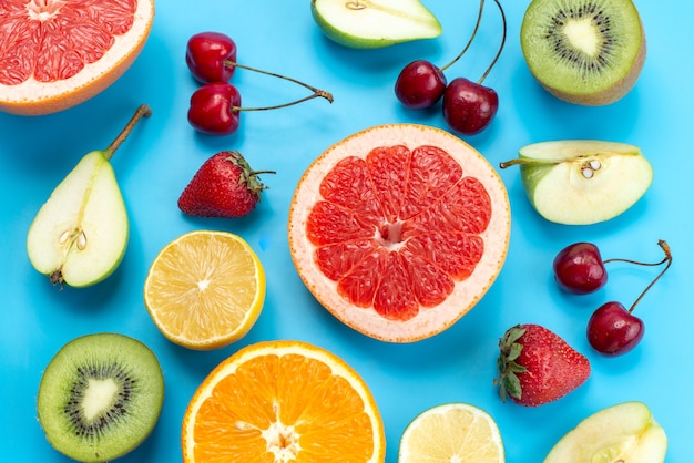 Une vue de dessus la composition de fruits colorés frais de fruits moelleux et tranchés sur bleu, couleur de vitamine de fruits