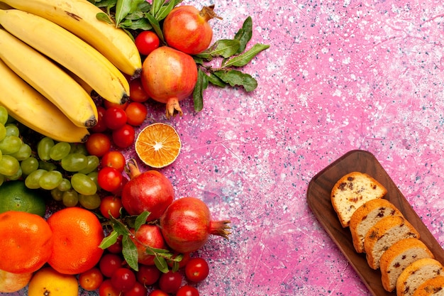 Photo gratuite vue de dessus de la composition de fruits frais avec des gâteaux en tranches sur un bureau rose clair