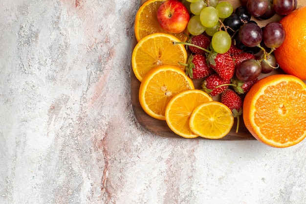 Vue de dessus de la composition de fruits frais oranges raisins et fraises sur une surface blanc clair