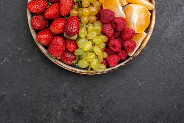 Vue de dessus de la composition des fruits fraises raisins framboises et mandarines à l'intérieur du plateau sur l'espace sombre