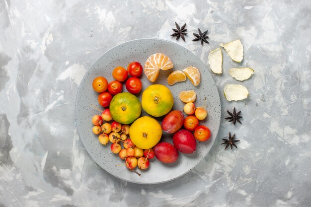 Vue de dessus composition de fruits mandarines cerises prunes à l'intérieur de la plaque sur fond gris clair.