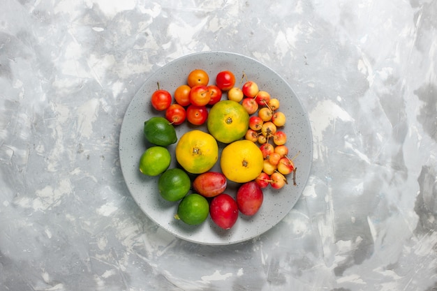 Vue de dessus composition de fruits mandarines citrons prunes à l'intérieur de la plaque sur le bureau gris clair.