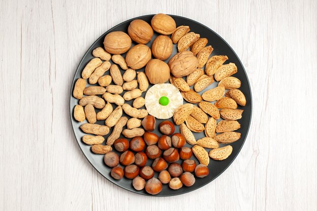 Vue de dessus composition de noix noix fraîches cacahuètes et noisettes à l'intérieur de la plaque sur un bureau blanc casse-croûte de noix arbre de nombreuses coquilles