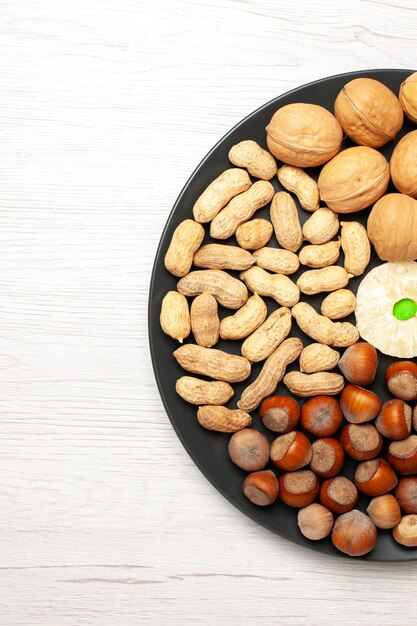 Vue de dessus composition des noix noix fraîches cacahuètes et noisettes à l'intérieur de la plaque sur un bureau blanc clair écrou snack plante arbre beaucoup de coquille