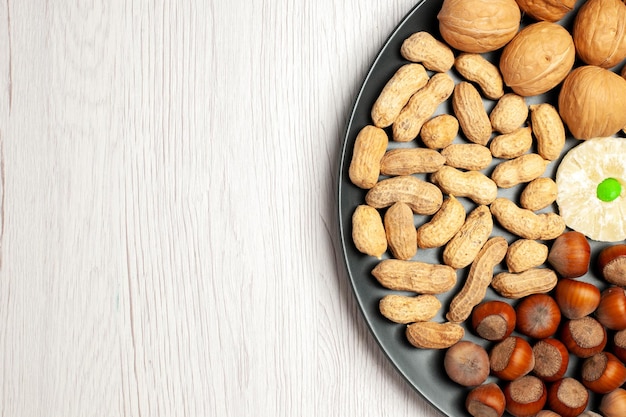 Vue de dessus composition des noix noix fraîches cacahuètes et noisettes à l'intérieur de la plaque sur un bureau blanc noix snack plante arbre beaucoup de coquille