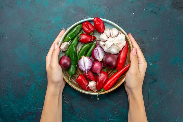 Vue de dessus de la composition végétale oignons ail poivrons touchés par femme sur la table sombre salade de légumes couleur repas alimentaire