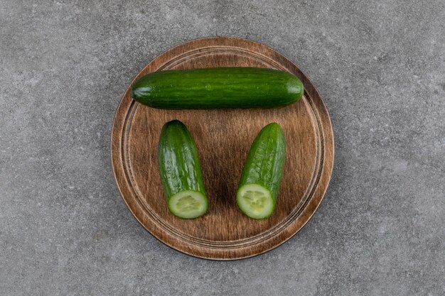 Vue de dessus de concombres frais entiers ou à moitié coupés sur planche de bois.