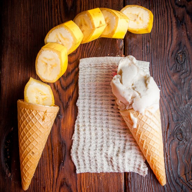 Vue de dessus des cônes de gaufre avec de la glace à la banane et des tranches de banane dans des serviettes en chiffon