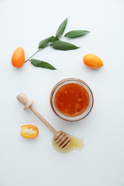 Vue de dessus de la confiture de coings dans un bocal en verre et des kumquats avec une louche à confiture sur fond blanc