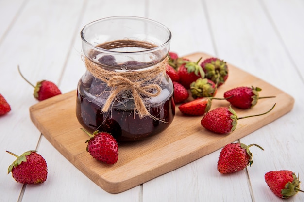 Vue de dessus de la confiture de fraises sur une planche de cuisine en bois avec des fraises fraîches sur un fond en bois blanc