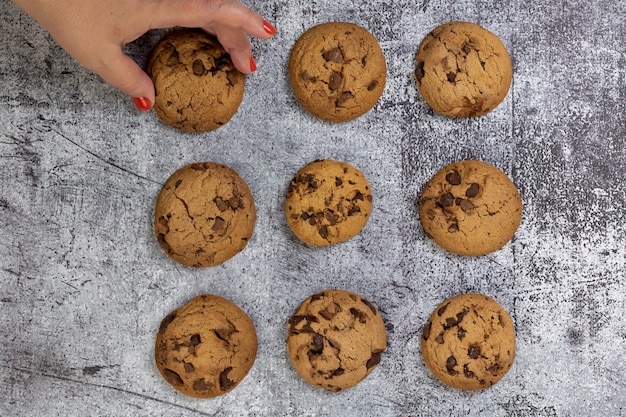 Vue de dessus des cookies aux pépites de chocolat sur une surface texturée avec une femme prenant un cookie