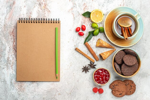 Vue de dessus des cookies une tasse de thé noir au citron cannelle confiture de citrons anis étoilé cahier et crayon