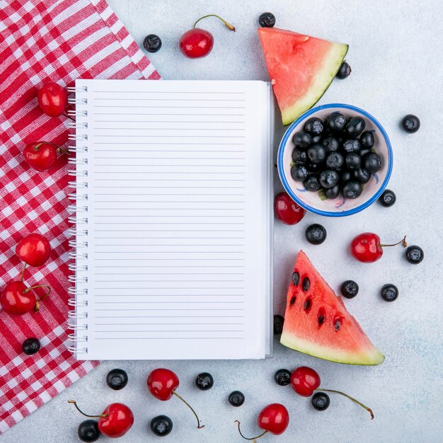 Vue de dessus copie espace cahier avec des tranches de pastèque aux cerises et myrtilles dans une tasse