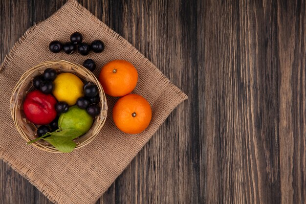 Vue de dessus copie espace cerise prune avec citron lime et pêche dans un panier d'oranges sur un fond en bois