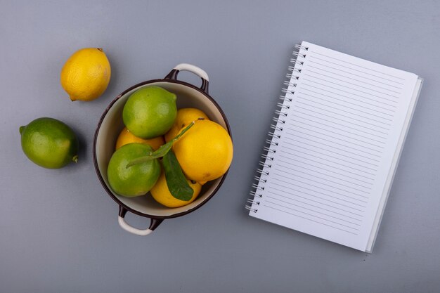 Vue de dessus copie espace citrons avec limes dans une casserole avec bloc-notes sur fond gris