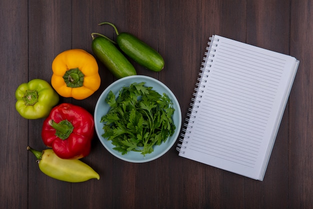 Vue de dessus copie espace copybook avec du persil dans un bol avec des concombres et des poivrons sur fond de bois