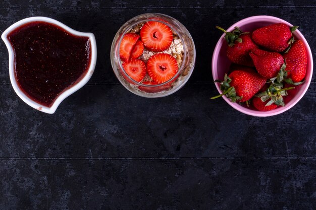 Vue de dessus copie espace granola aux fruits et noix dans un verre avec des fraises dans un bol rose et de la confiture