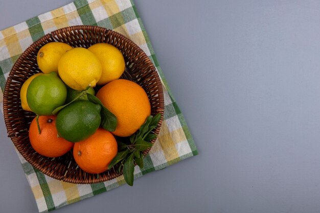 Vue de dessus copie espace oranges aux citrons et limes dans un panier sur une serviette à carreaux jaune sur fond gris