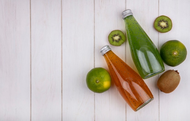 Photo gratuite vue de dessus copiez les bouteilles de jus de l'espace avec des mandarines et des kiwis sur un mur blanc