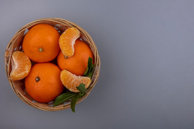 Vue de dessus copiez les oranges de l'espace avec des cales pelées dans un panier sur un fond gris