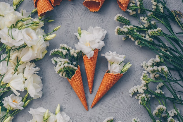 Vue de dessus des cornets de crème glacée avec des fleurs sur gris clair