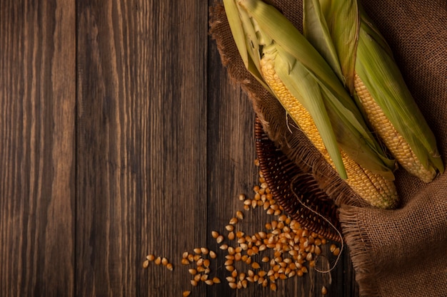 Photo gratuite vue de dessus des cors frais bio avec des cheveux sur un seau en tissu sac avec des noyaux isolé sur une table en bois avec espace copie