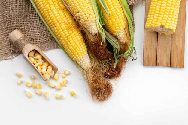 Une vue de dessus les cors jaunes crus avec des feuilles vertes sur un bureau blanc, le maïs de couleur repas alimentaire