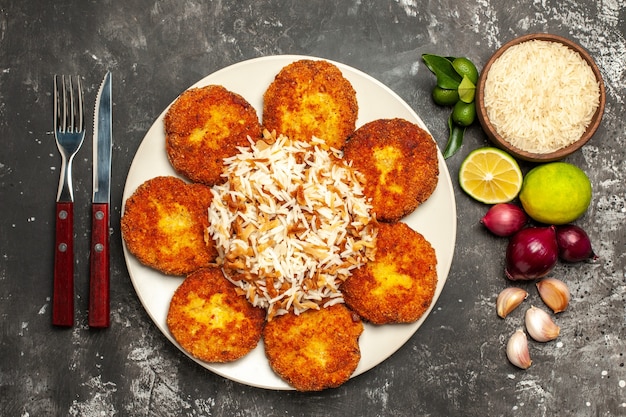 Vue de dessus côtelettes frites avec du riz cuit sur la surface sombre plat alimentaire viande rissole