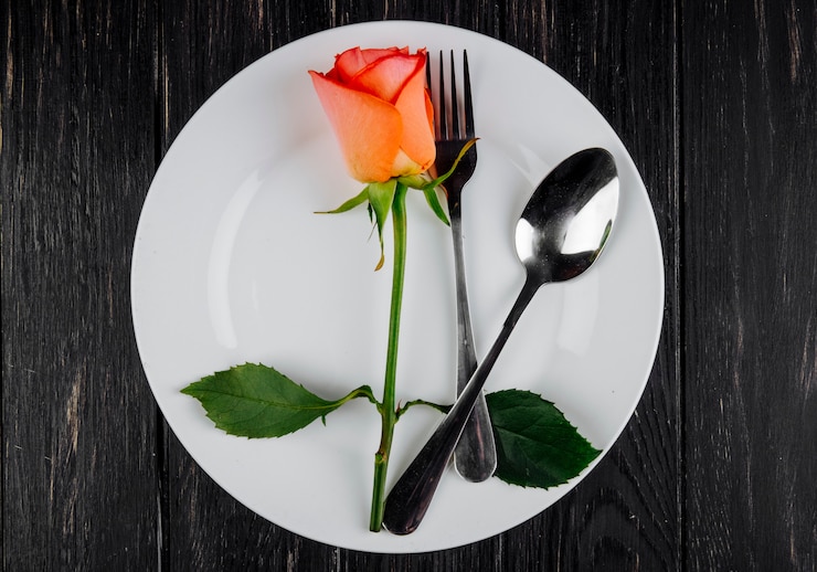 Photo gratuit vue de dessus de couleur orange rose avec cuillère et fourchette sur une plaque blanche sur fond de bois foncé