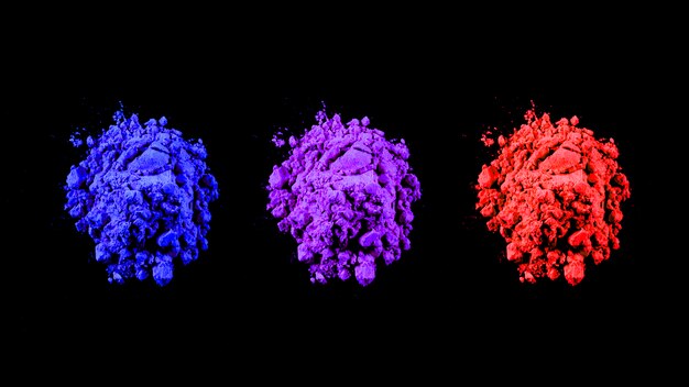 Vue de dessus des couleurs holi rouges, bleus et violets disposés en rangée sur fond noir