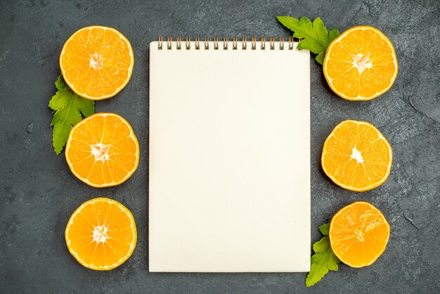 Vue de dessus couper des oranges un cahier sur fond sombre