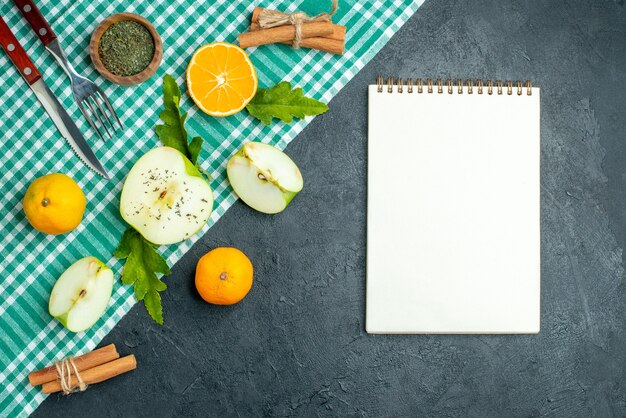 Vue de dessus couper les pommes et les mandarines des bâtons de cannelle attachés avec un couteau à corde et une fourchette sur une nappe verte